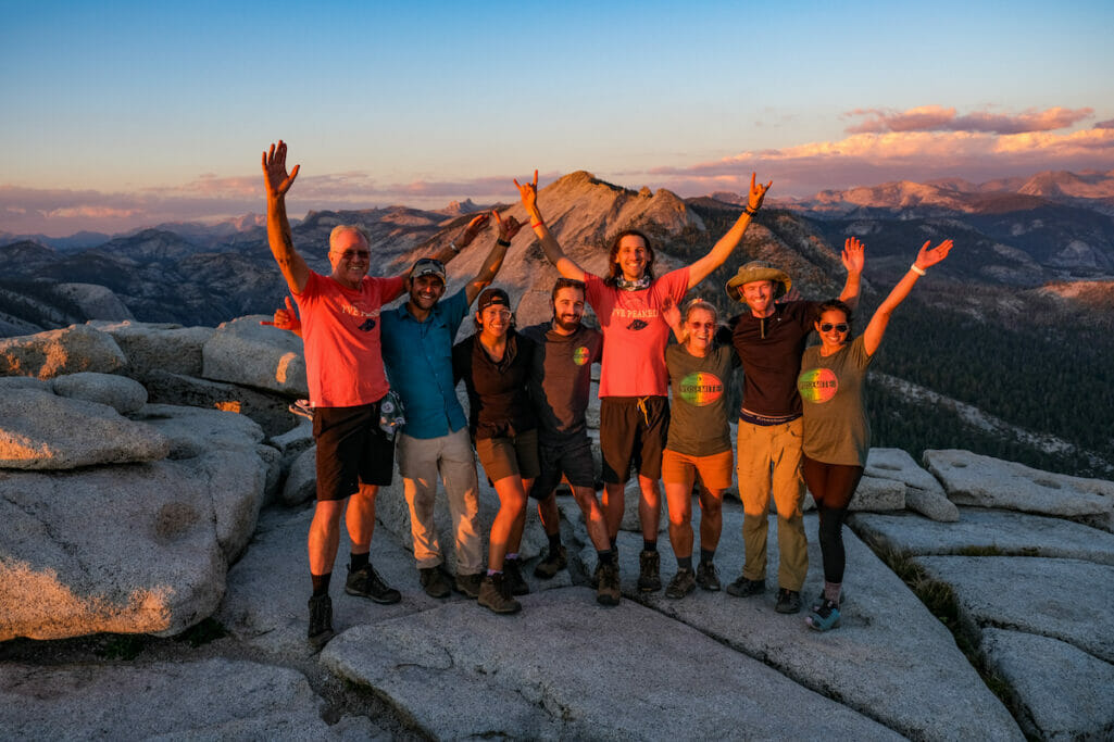 Family celebrating on top of Half Dome while the sun is setting.