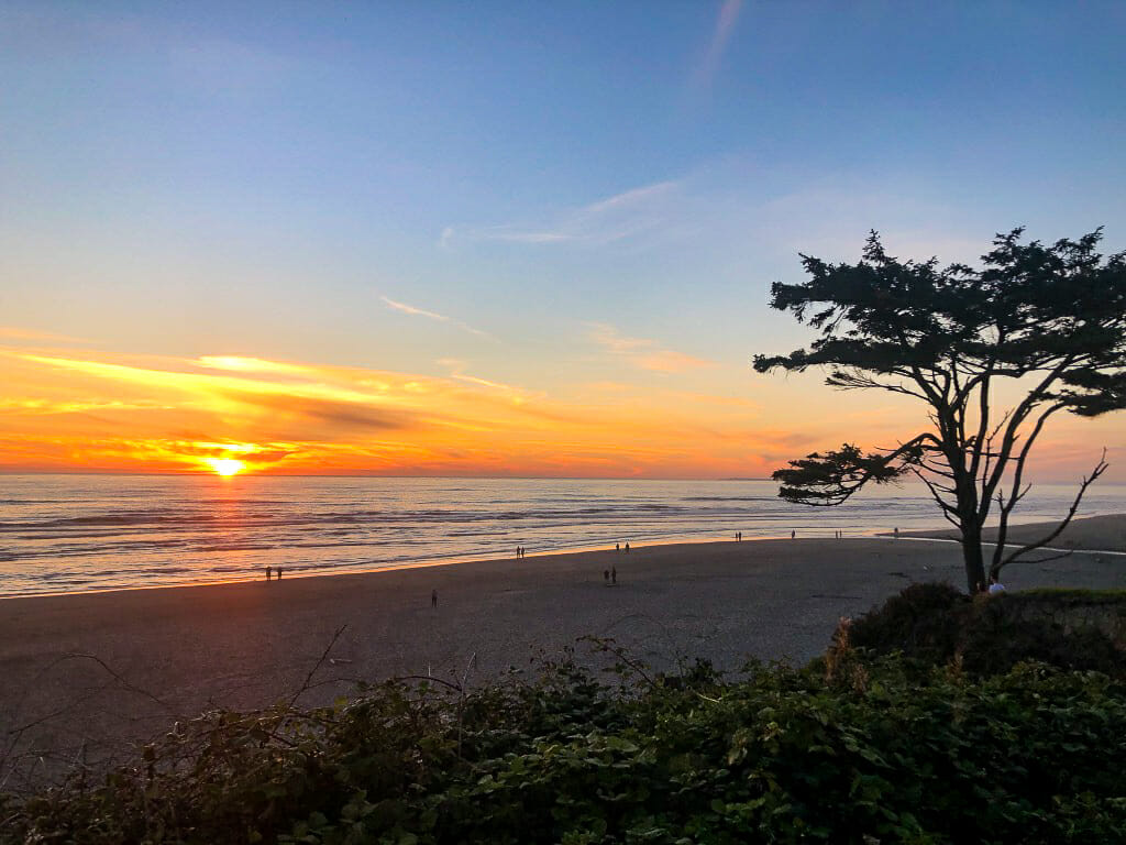Sunset at the beach at Kalaloch with people walking on the sand in Olympic National Park.