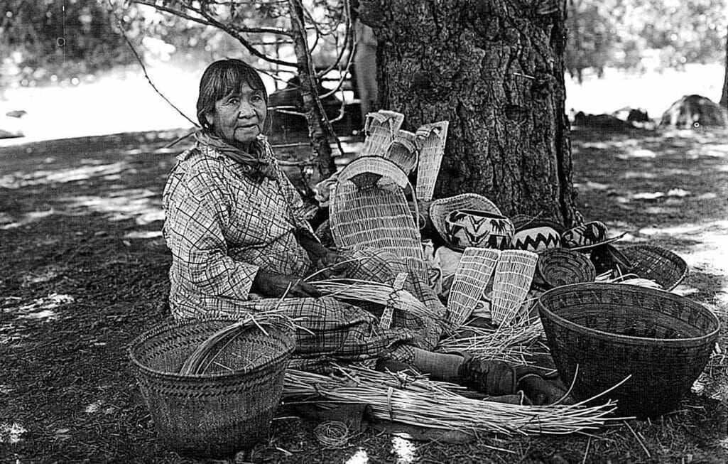 Maggie Howard sits with her baskets and supplies to weave them by a tree in Yosemite Valley.