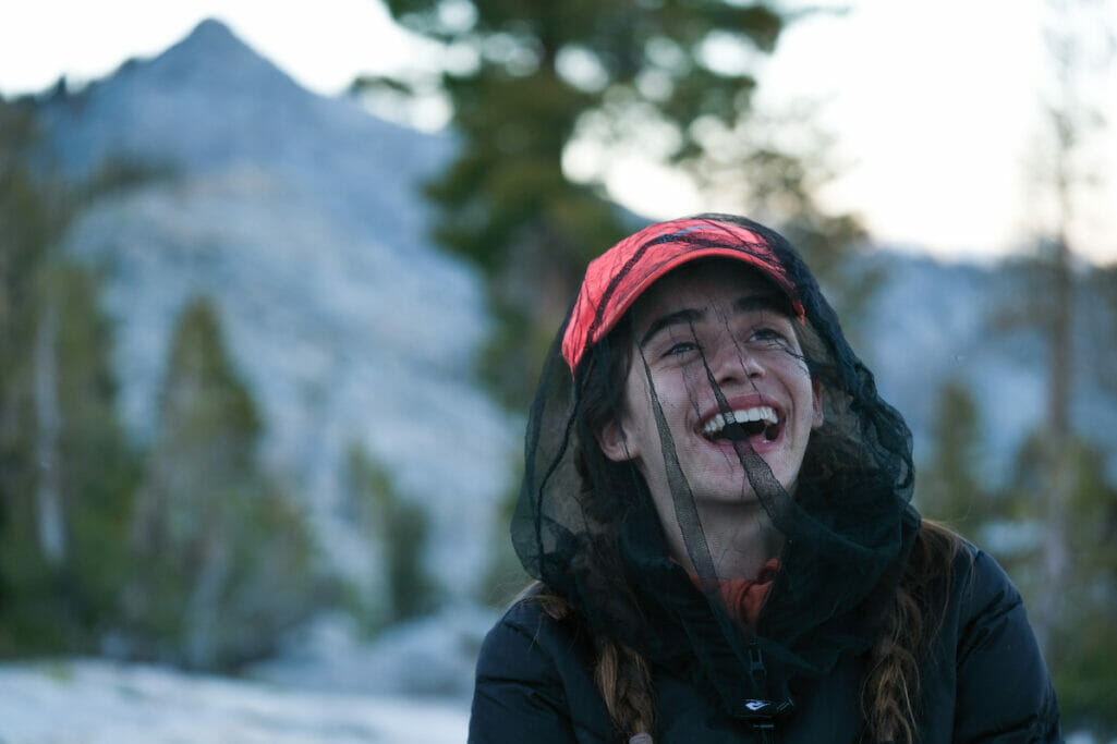 A girl wearing a mosquito head net laughs.