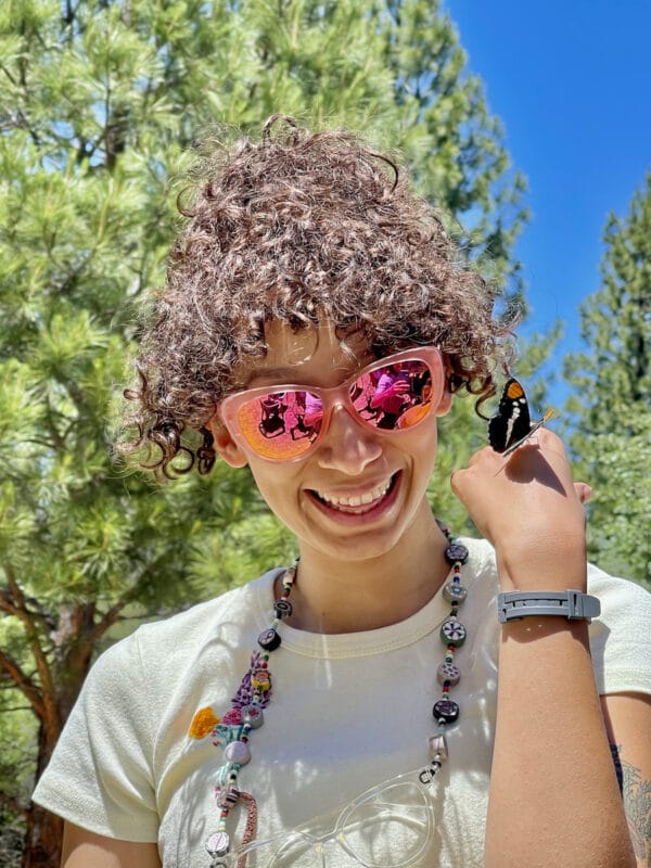Woman wearing Goodr sunglasses with a butterfly on her hand.