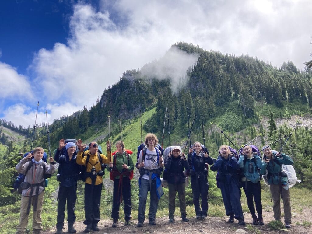 Kids reaching high with their trekking poles in front of a mountain in Olympic National Park.