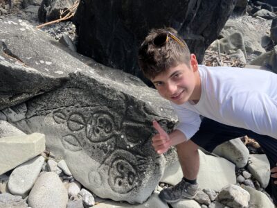 Teen boy giving a thumbs up next to native rock art