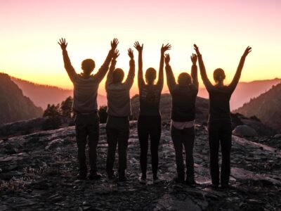 A group of teens with their hands up in the air for sunset
