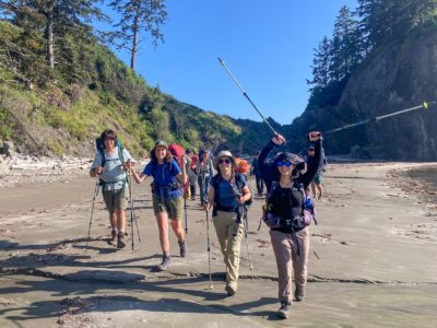 Teen backpackers celebrating with trekking poles on the coast in Olympic National Park