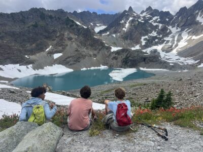 Three backpackers looking at a blue lake and mountains in Olympic National Park